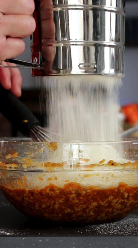 de bloemix (vaste ingrediënten om pompoencupcakes te maken) door een zeef gebruiken om eventuele klontjes te verwijderen