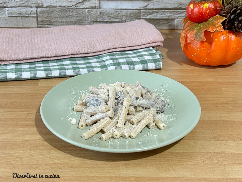 Bord met korte pasta met ricottasaus en gesauteerde champignons, geserveerd op een groen bord met geraspte Parmezaan