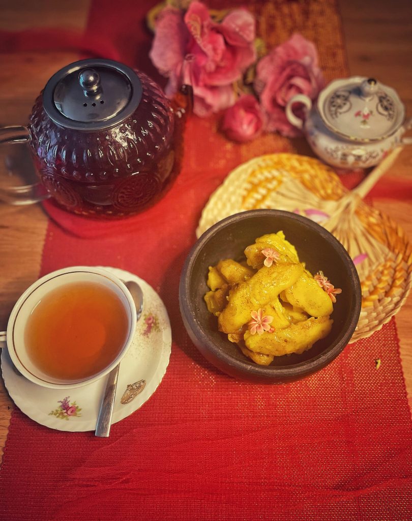 Close-up van knapperige Bananenfritters uit Sri Lanka, goudbruin geserveerd op een bord met een stomende glazen theepot op de achtergrond