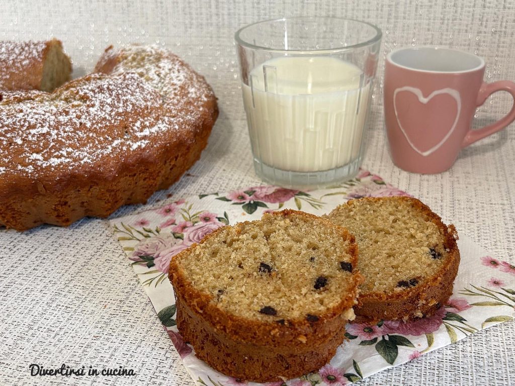 Plakken ciambellone met melk en koffie en chocoladedruppels, geserveerd met een glas melk en een kopje koffie op een bloemenservet.