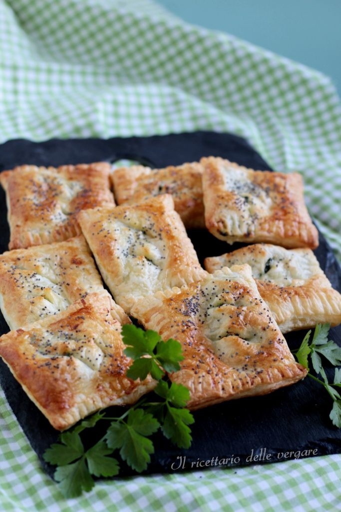 Acht goudbruine bladerdeegpakketjes gevuld met ricotta en spinazie, gerangschikt op een donker bord met verse spinazieblaadjes