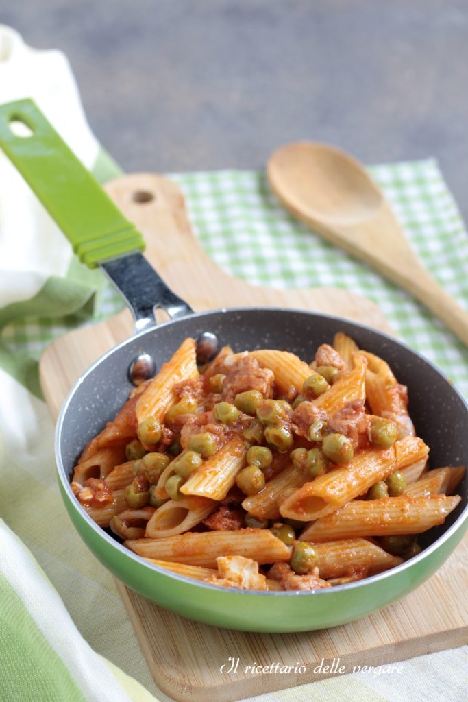 Verticale close-up van korte pasta in tomatensaus en doperwten in een groene pan.
