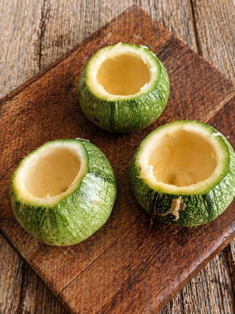 Ronde courgettes uitgehold met lepel op houten snijplank