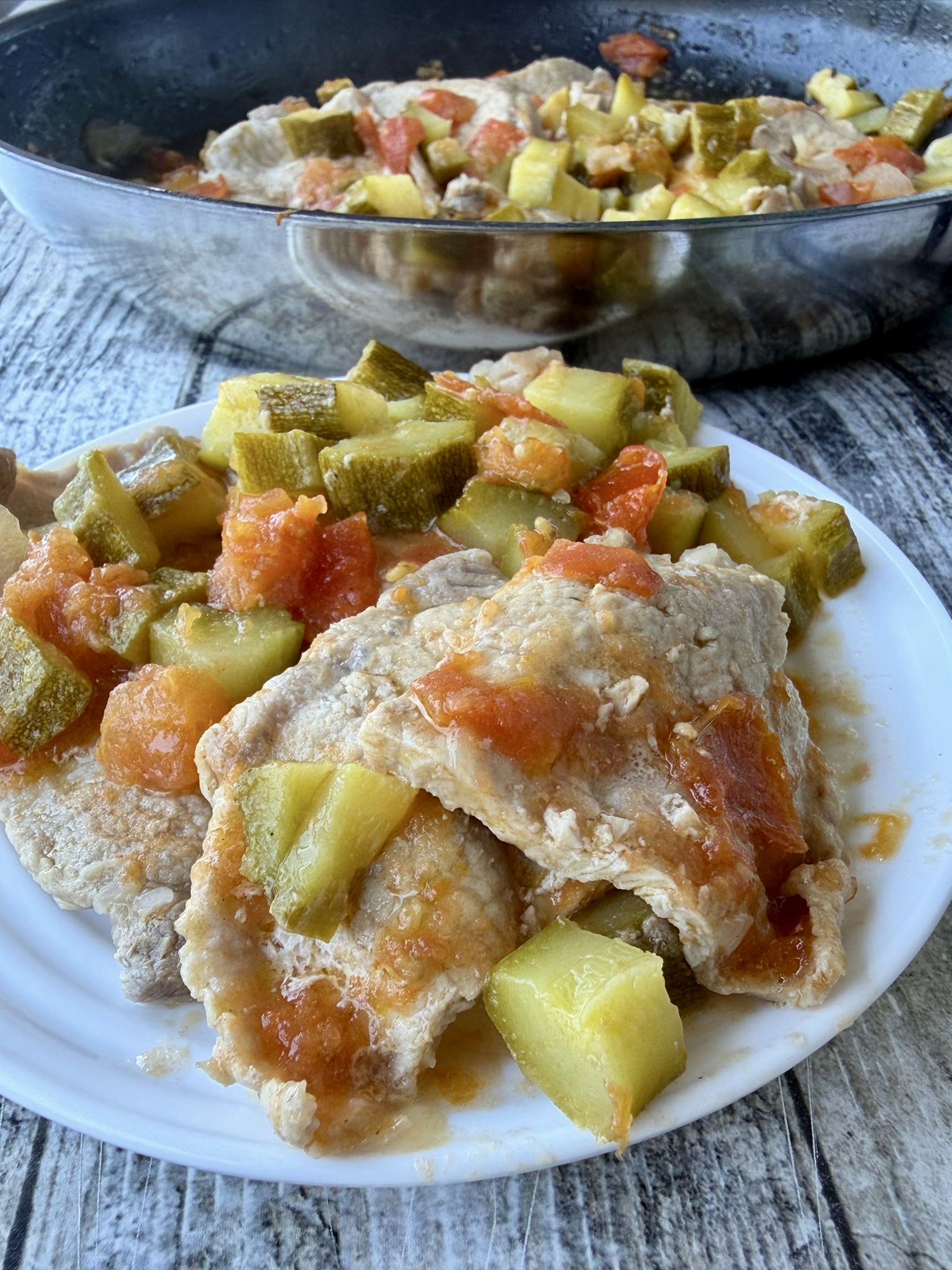 Plakjes varkenslende in de pan met courgette en tomaten