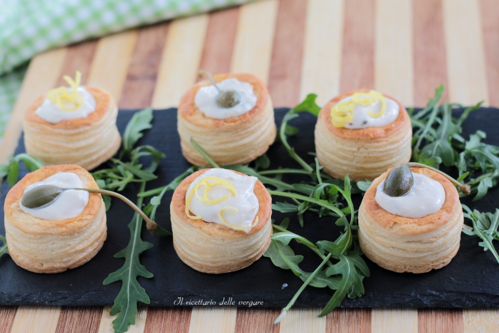 Schaal met vol-au-vent gevuld met tonijnmousse en kappertjes, geserveerd op een bedje van verse rucola.