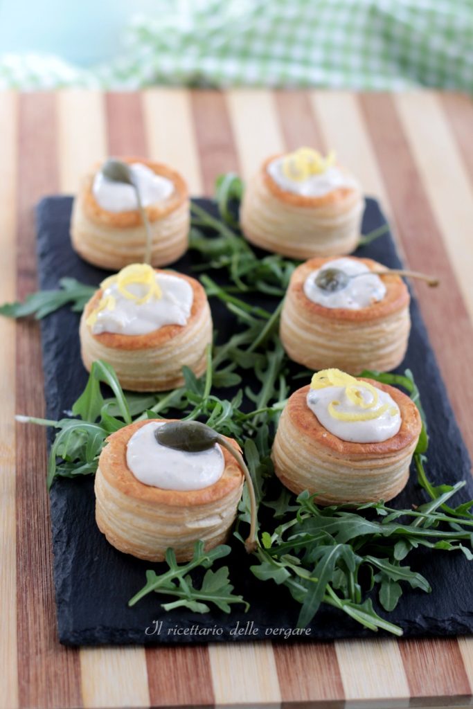 Zes vol-au-vent van bladerdeeg verticaal gerangschikt op een donker snijplank, gevuld met tonijnmousse en gegarneerd met verse kruiden.