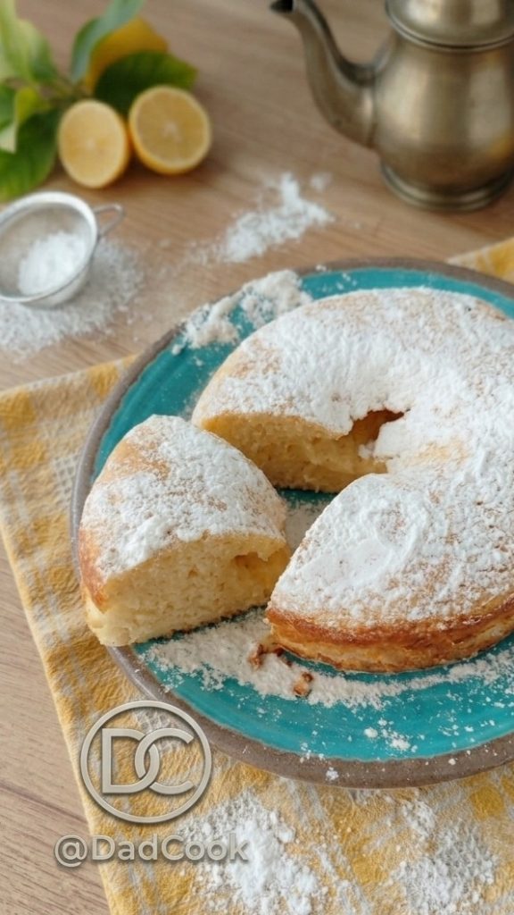 Close-up opname van een stuk zachte citroen-yoghurtcake met geitenkaas, gegarneerd met verse citroenrasp.